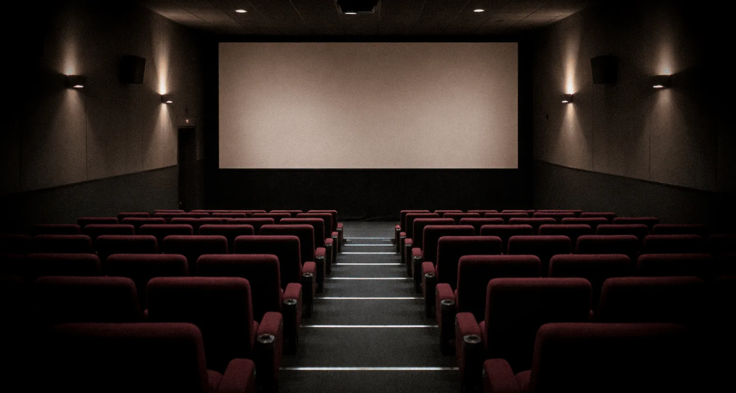 Salle de cinéma aux fauteuils rouges disposés en gradins face à un grand écran blanc éclairée par une lumière tamisée